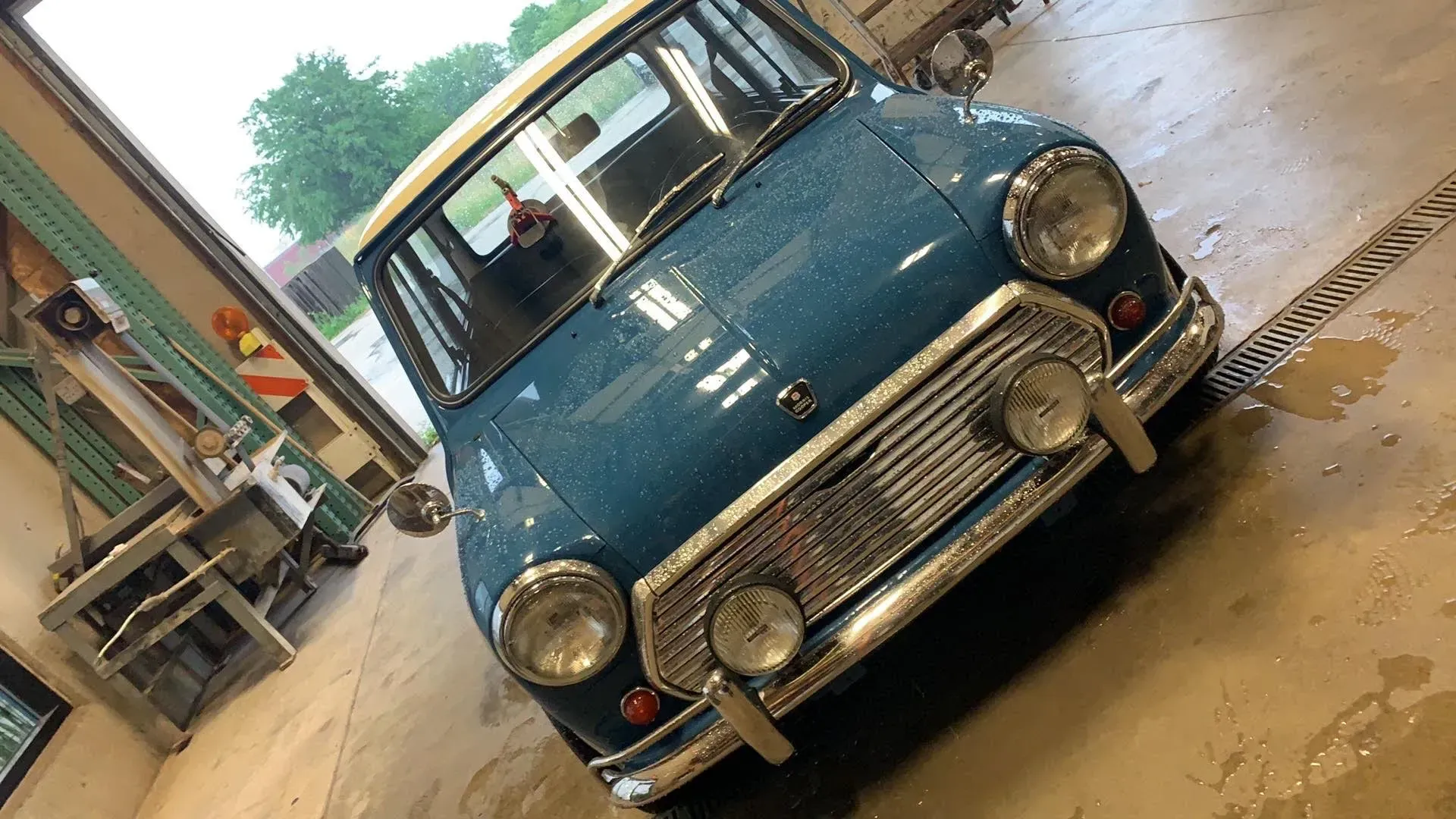 A blue Mini Cooper with a white roof parked inside a workshop with a light-colored concrete floor.
