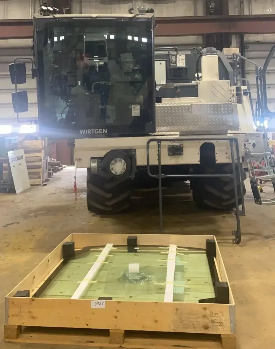 A white heavy-duty vehicle parked in a workshop next to a wooden crate containing a large sheet of flat glass.