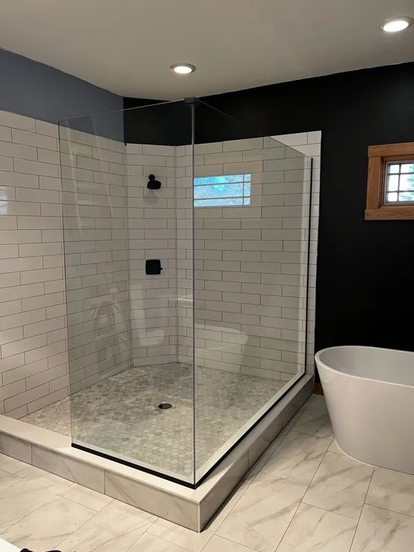 A modern bathroom featuring a glass-enclosed shower with white subway tiles and a freestanding tub against a black wall.