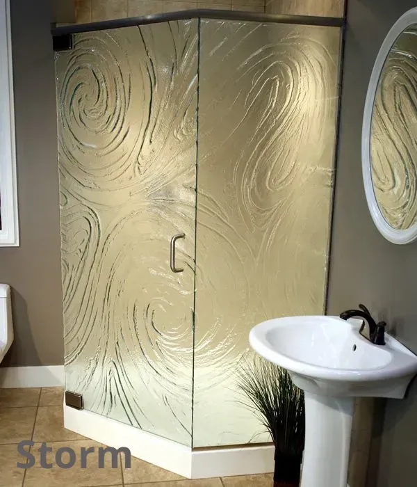 Neo-angle shower enclosure with textured glass featuring a swirling pattern, next to a pedestal sink in a bathroom.