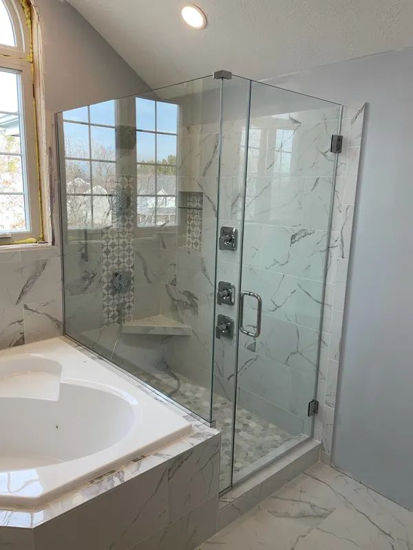 Modern bathroom featuring a glass-enclosed shower with marble-style tiles and a soaking tub in the foreground.