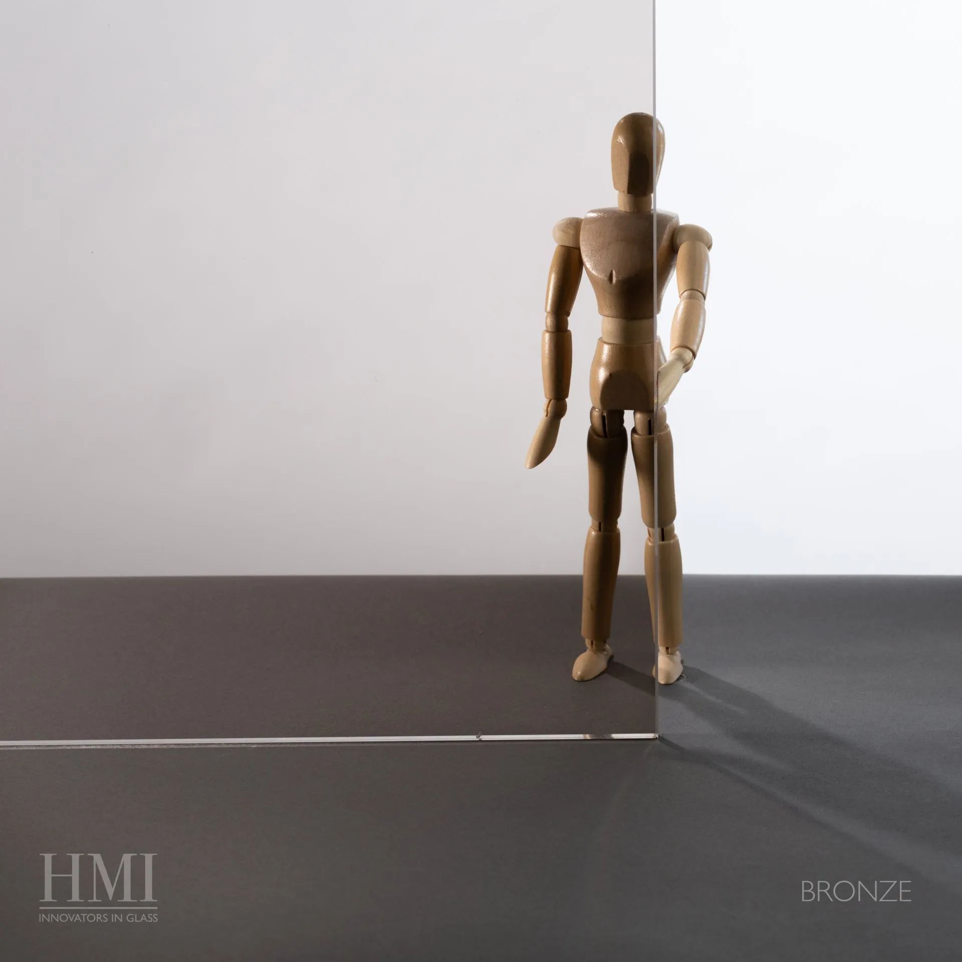 A small wooden artist's mannequin stands behind a sheet of semi-transparent bronze-tinted glass.