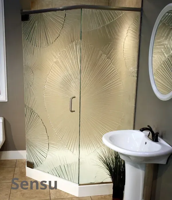 A corner shower stall with patterned glass featuring circular, fan-like radial designs in a bathroom with a pedestal sink.