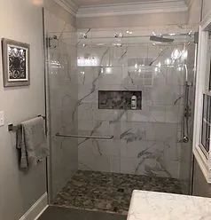 A modern walk-in shower with white marble-patterned tiles, a river stone floor, glass doors, and a built-in wall niche.