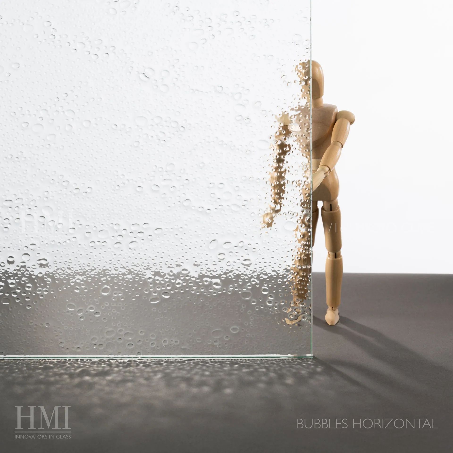 A wooden mannequin stands behind textured glass with a bubble pattern that obscures its left side.