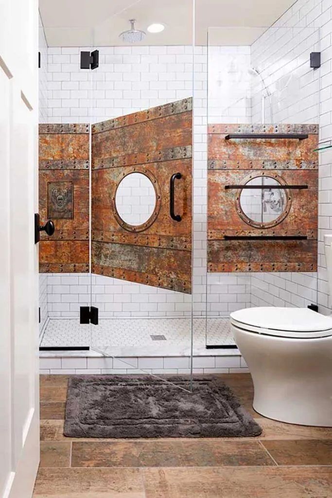 A glass shower enclosure features decorative rustic metal panels with circular porthole accents over white subway tiles.