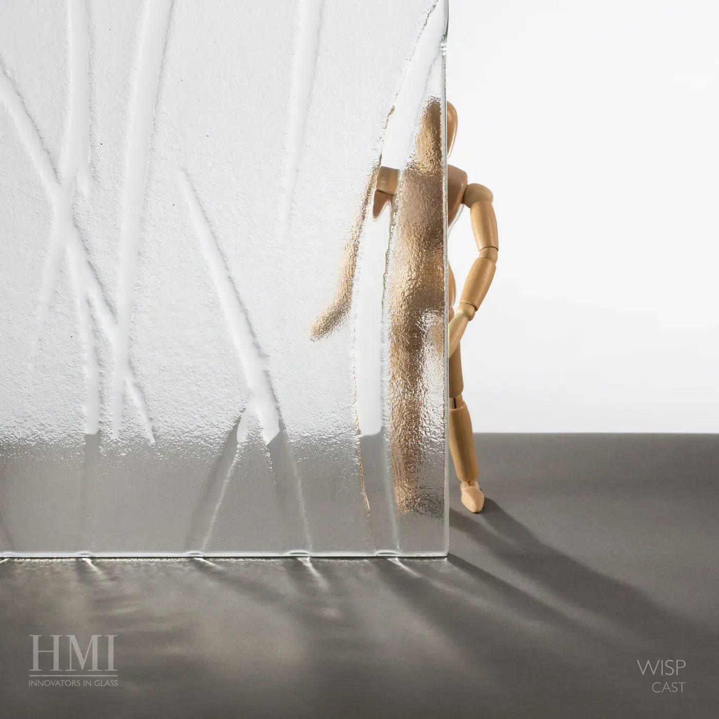 A small wooden mannequin stands partially behind a textured, patterned glass panel, casting a shadow on a flat surface.
