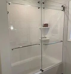 A modern glass sliding shower door installed over a white bathtub with built-in corner shelves.