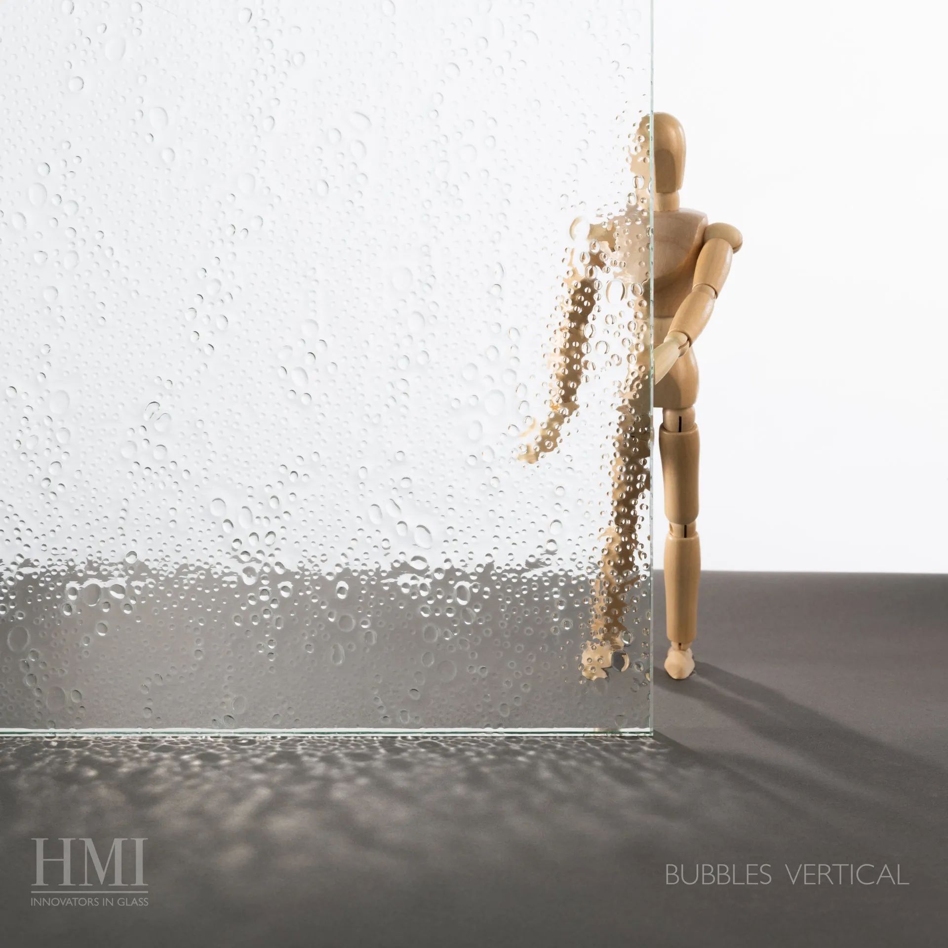 A wooden artist’s mannequin stands behind textured glass with a bubble pattern, which obscures half of its form.