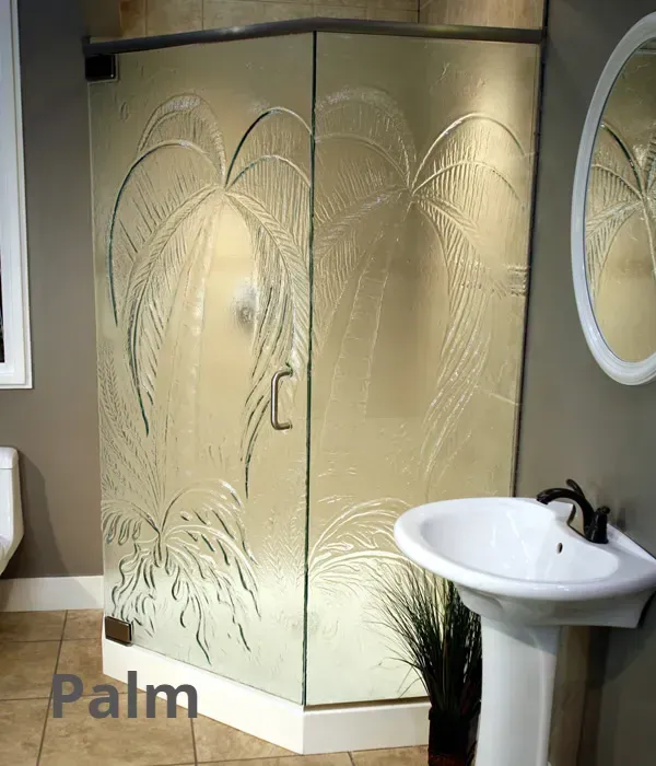 A corner shower enclosure in a bathroom with frosted glass featuring an etched palm tree design.