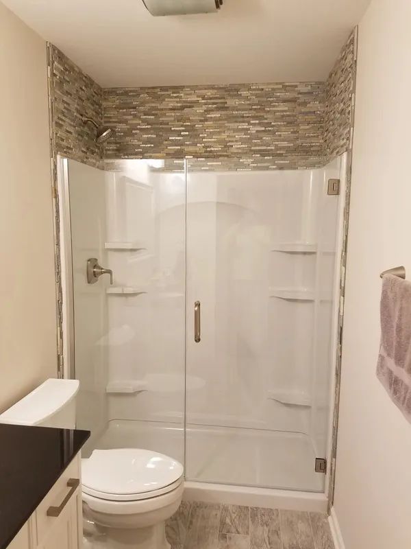 A bathroom featuring a glass-enclosed shower stall with a stone-tiled accent wall above it and a toilet to the left.