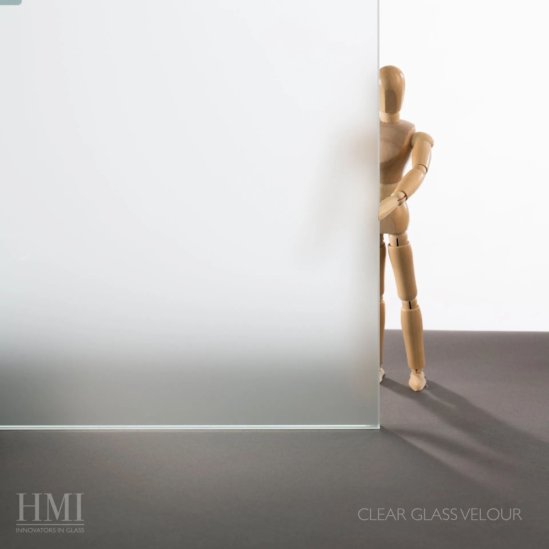 A wooden artist's mannequin stands behind a pane of frosted glass, partially obscured by the translucent surface.