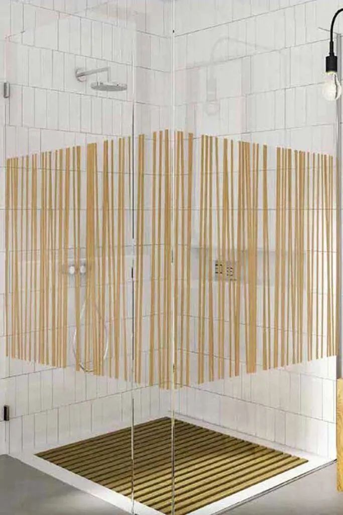 A modern glass shower enclosure with white tiled walls and a decorative brown, vertical-striped pattern on the glass.
