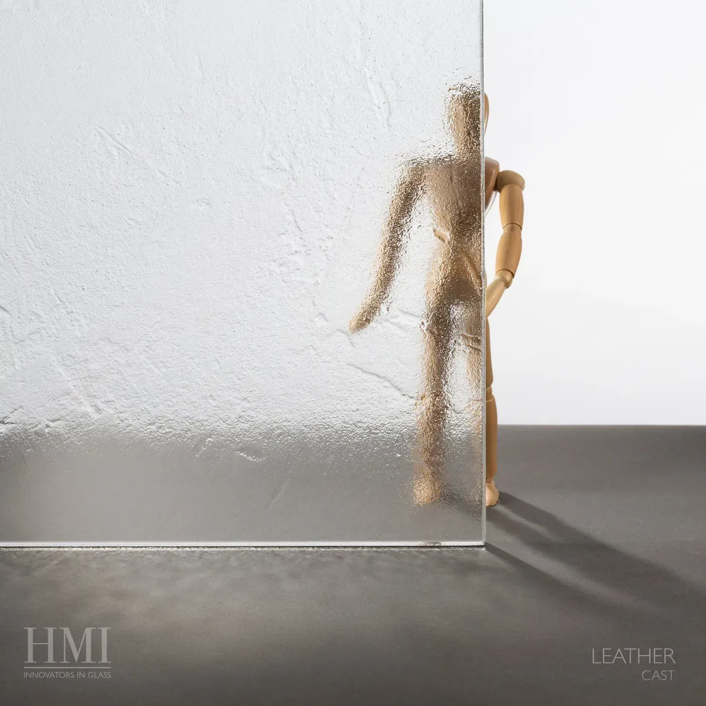 A sheet of textured, translucent glass obscures part of a small wooden mannequin figure standing on a dark surface.