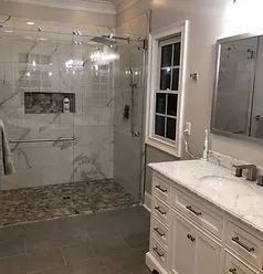A modern bathroom featuring a white marble vanity, a glass-enclosed shower with pebble floor, and a framed window.