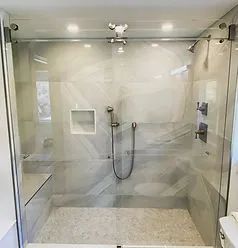 A glass-enclosed shower with light-toned marble tile walls, a handheld showerhead, and a recessed storage niche.