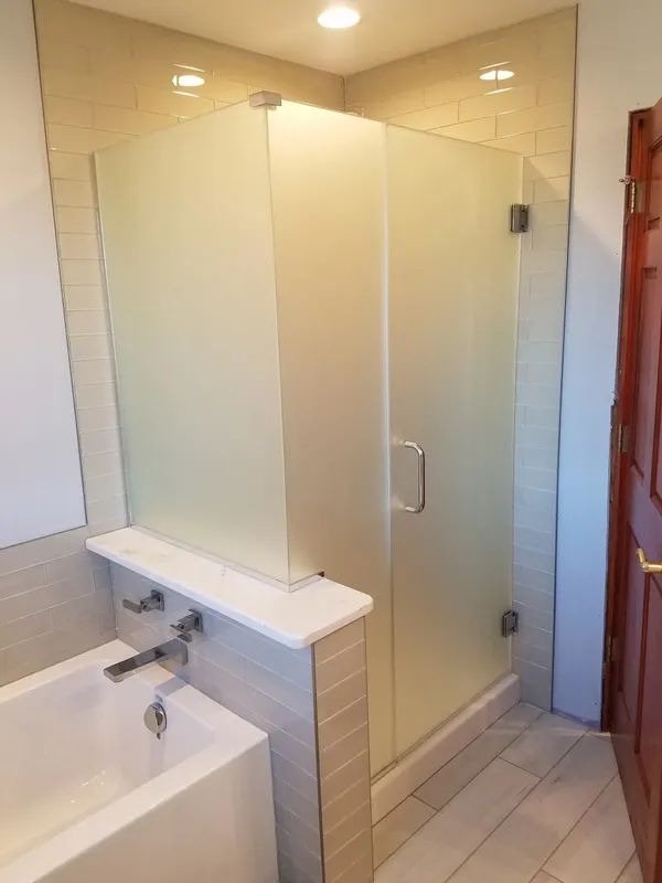 A modern bathroom featuring a white bathtub, a tiled half-wall ledge, and a walk-in shower with a frosted glass door.