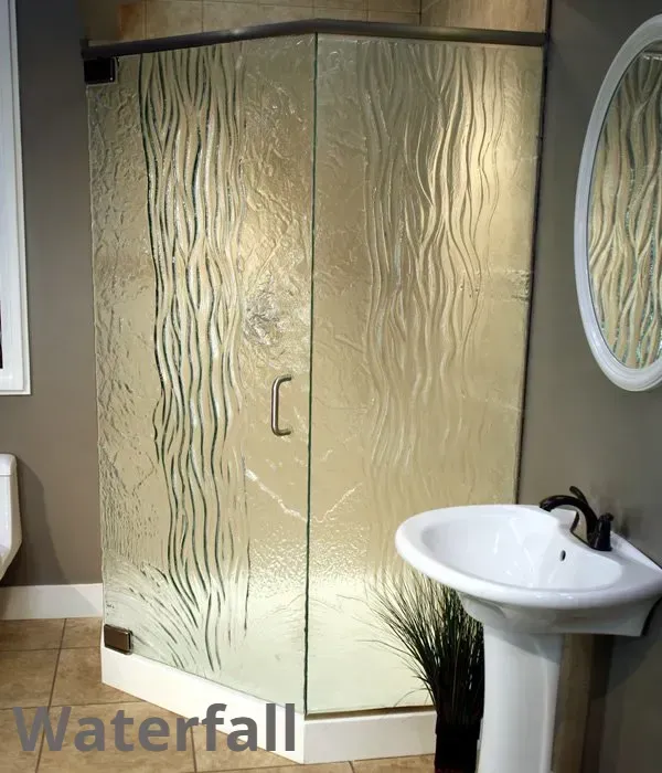 A corner shower stall featuring glass panels with a textured, flowing vertical pattern, next to a white pedestal sink.