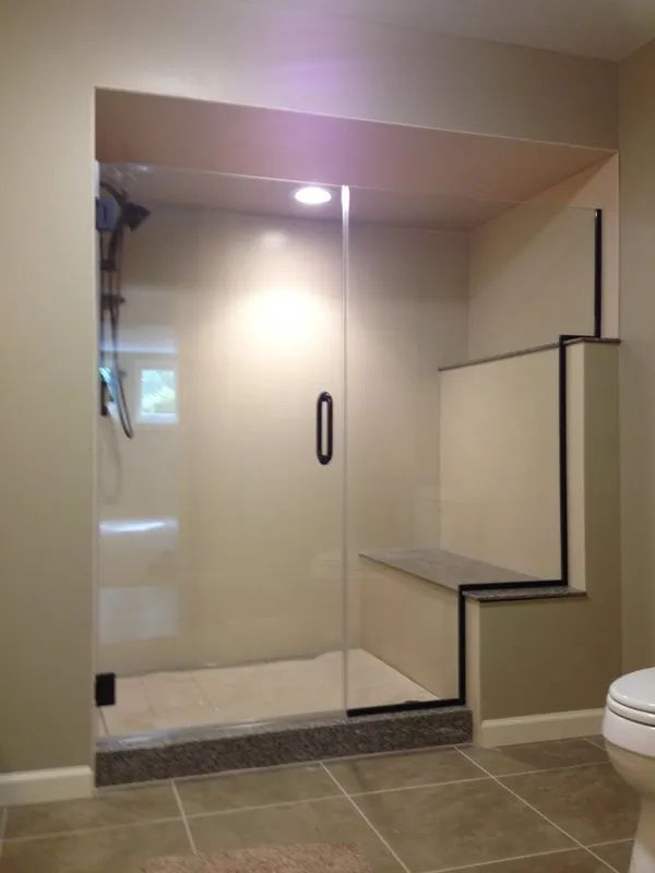 Walk-in shower with a glass door, built-in bench, and neutral-colored tile in a modern bathroom setting.
