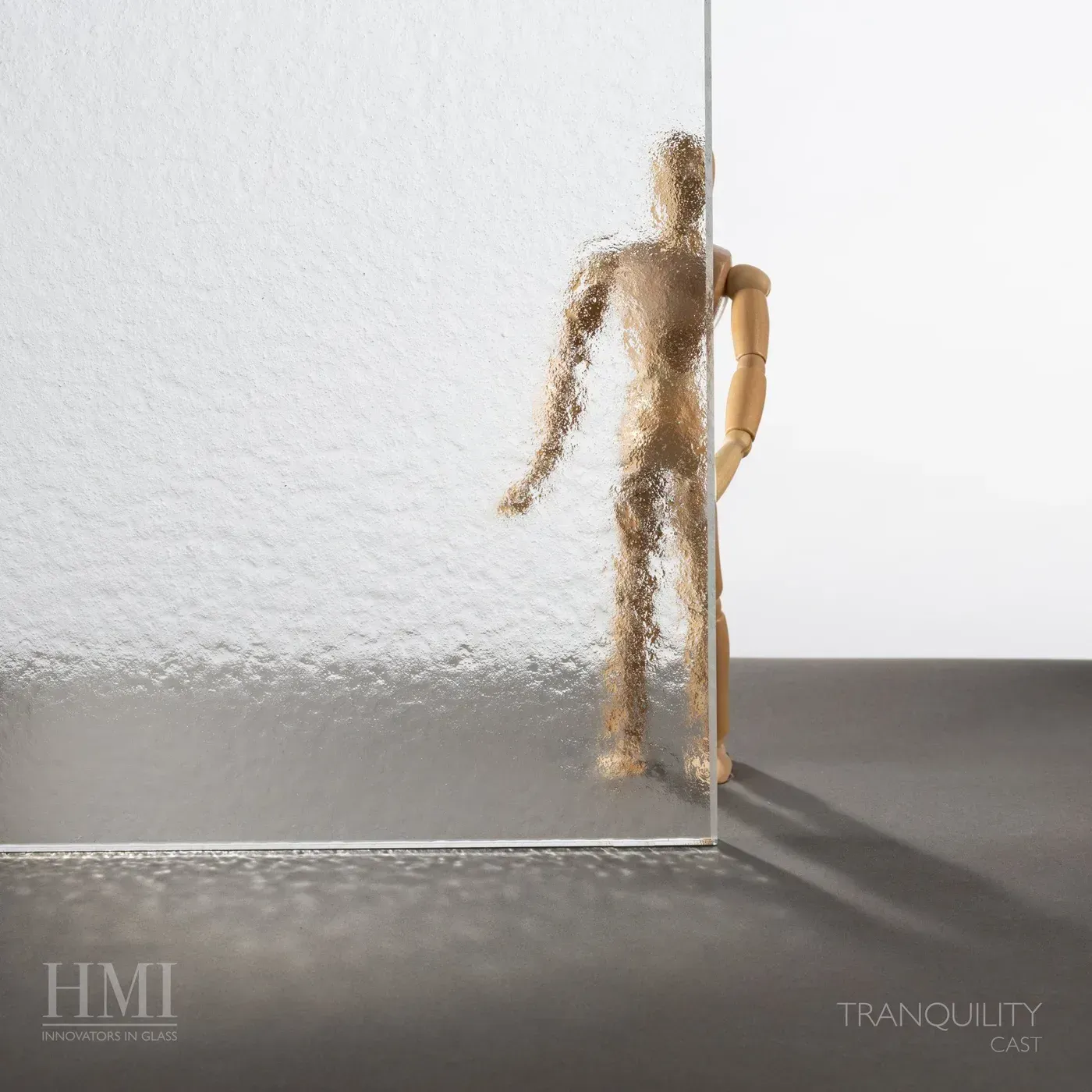 A wooden mannequin stands partially behind a textured, semi-opaque glass pane, which obscures half of its body.