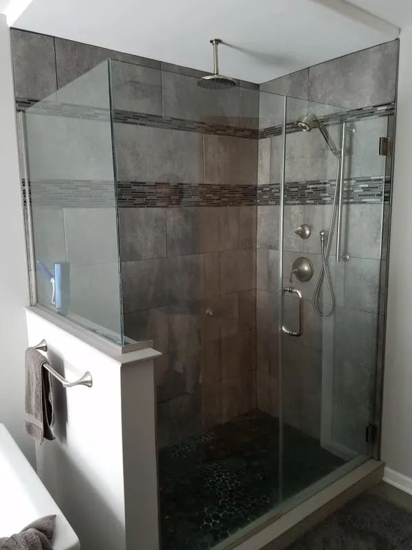 A glass-enclosed shower with tiled walls, an overhead rainfall showerhead, a handheld sprayer, and dark floor tiles.