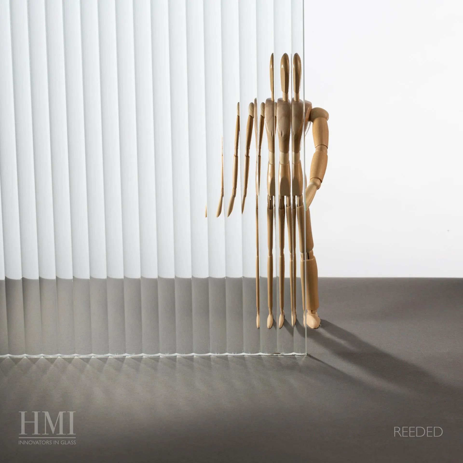 A wooden artist's mannequin stands behind reeded glass, creating a distorted, repeating reflection.