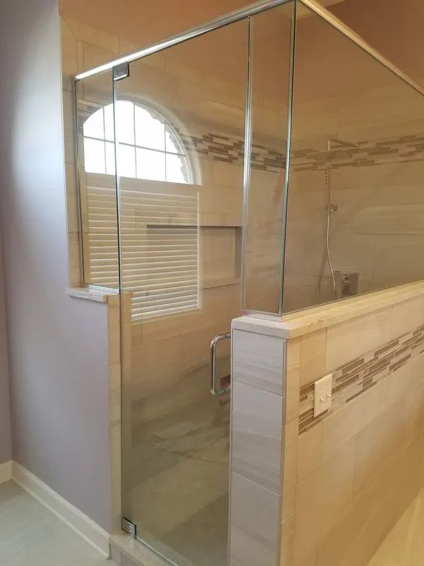 A modern bathroom with a glass shower enclosure, tiled half-walls, and an arched window with blinds.