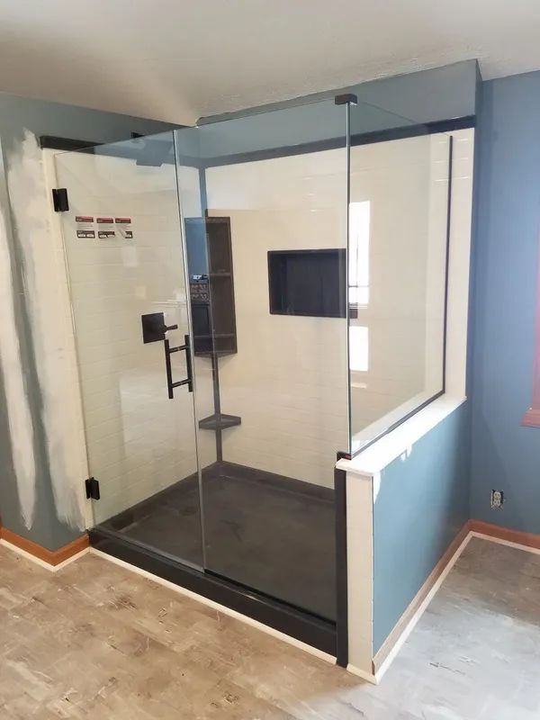 A walk-in shower with black hardware, a clear glass enclosure, and dark grey tile inside a room with blue walls.