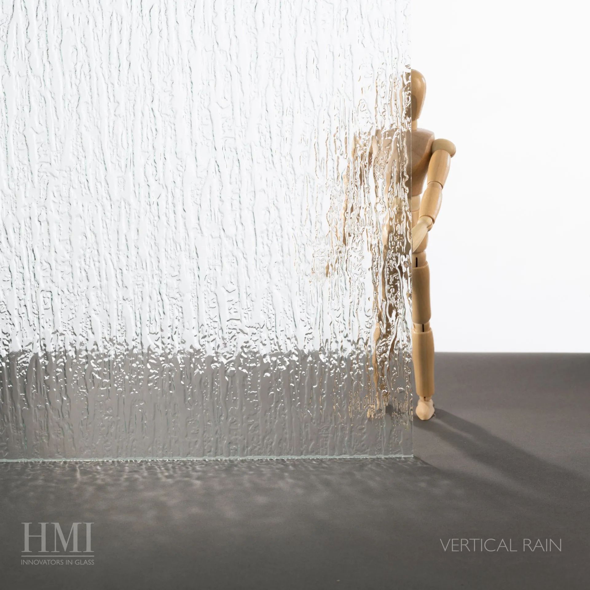 A sheet of glass with a vertical rain texture partially obscuring an artist's wooden mannequin figure.