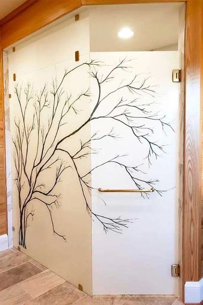 A glass shower enclosure with frosted panels featuring a black artistic tree branch design and a metal handle.