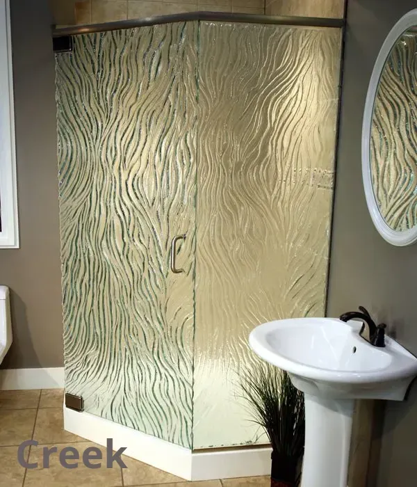 A corner shower stall with textured, wave-patterned glass panels, positioned next to a white pedestal sink in a bathroom.