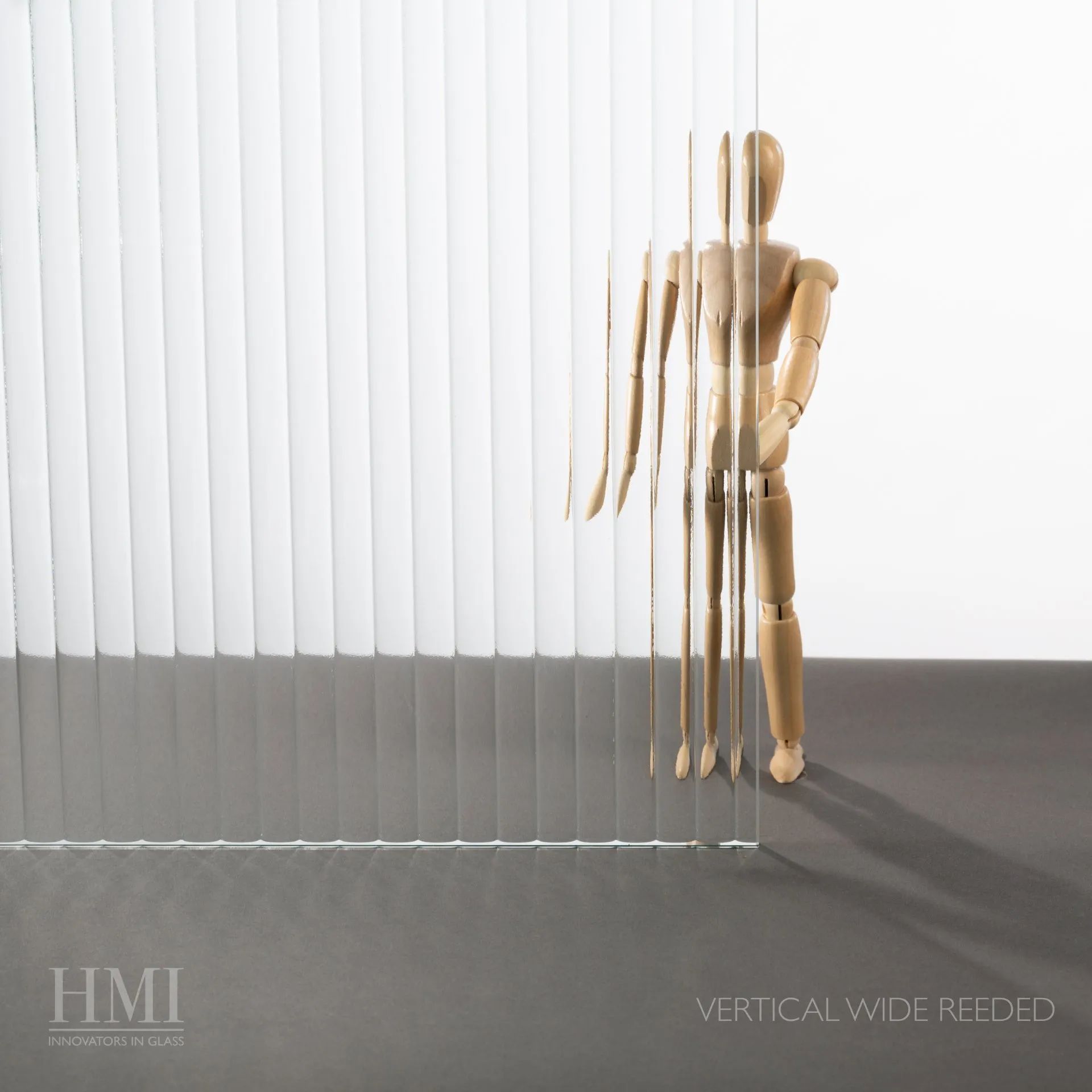 A wooden artist mannequin standing behind vertical wide-reeded glass, distorting its form.