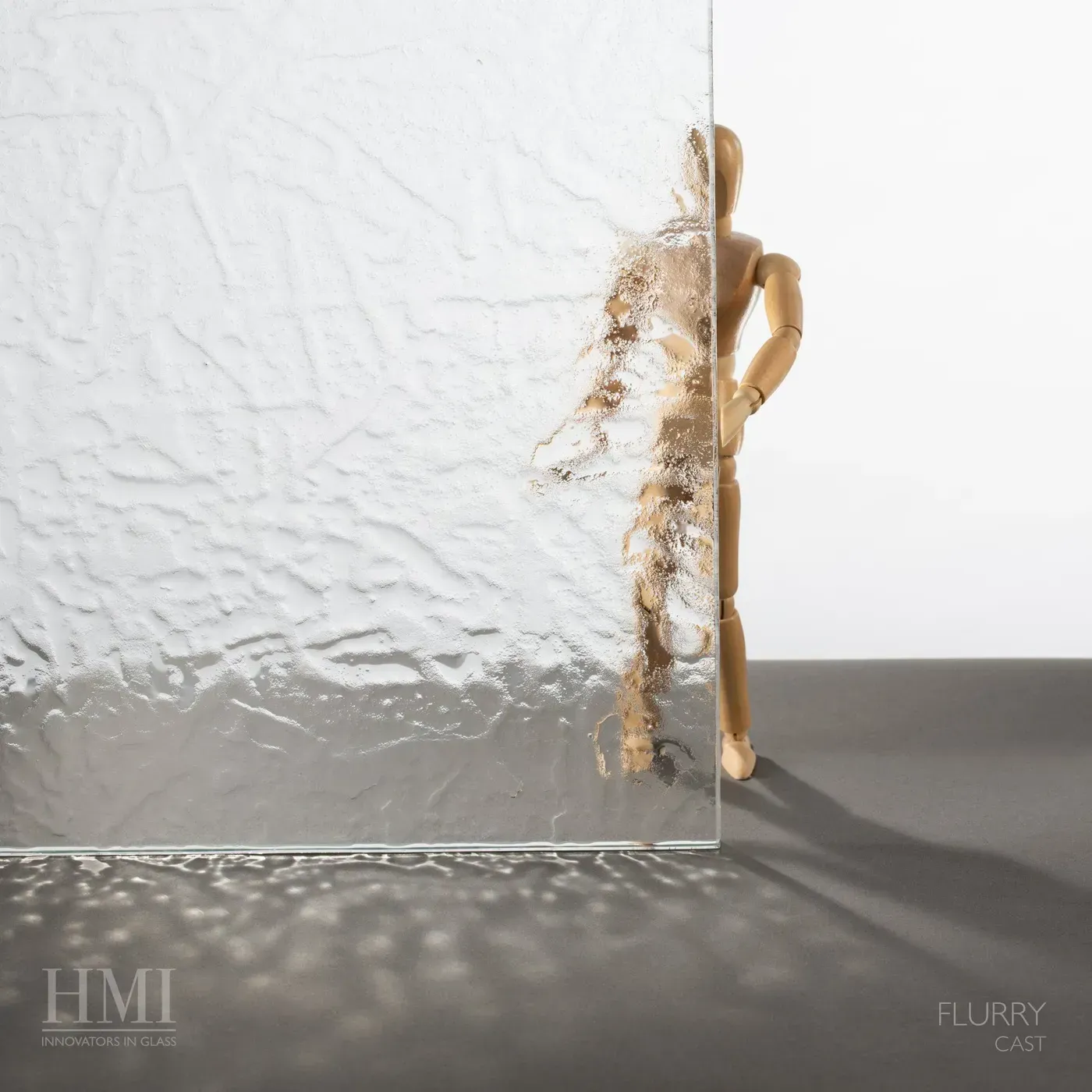 A piece of Flurry cast glass stands in front of a wooden mannequin, showing how the texture obscures the view behind it.