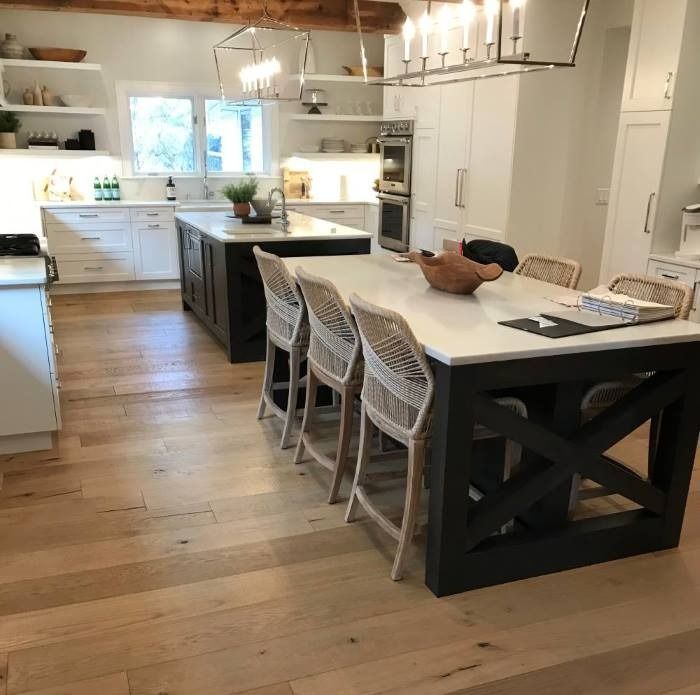 Spacious kitchen with a large island and seating, wood floors, white cabinets, and a second island in the background.