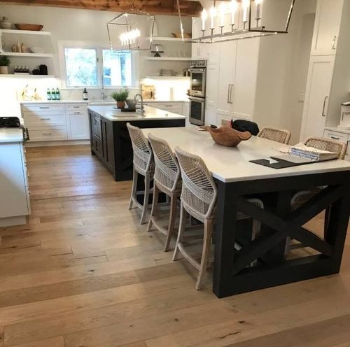 Spacious kitchen with a large island and seating, wood floors, white cabinets, and a second island in the background.