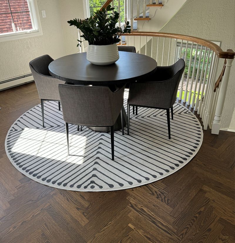 Round dining table with four chairs on a patterned rug, near a staircase with natural light.
