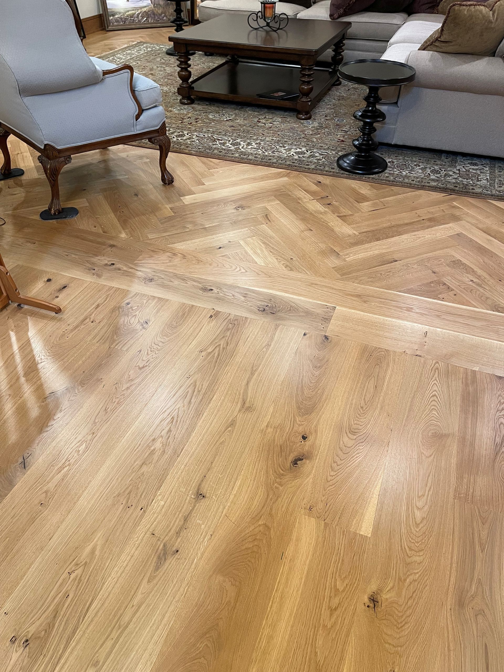 Light-colored wood flooring in a living room with a rug, and furniture