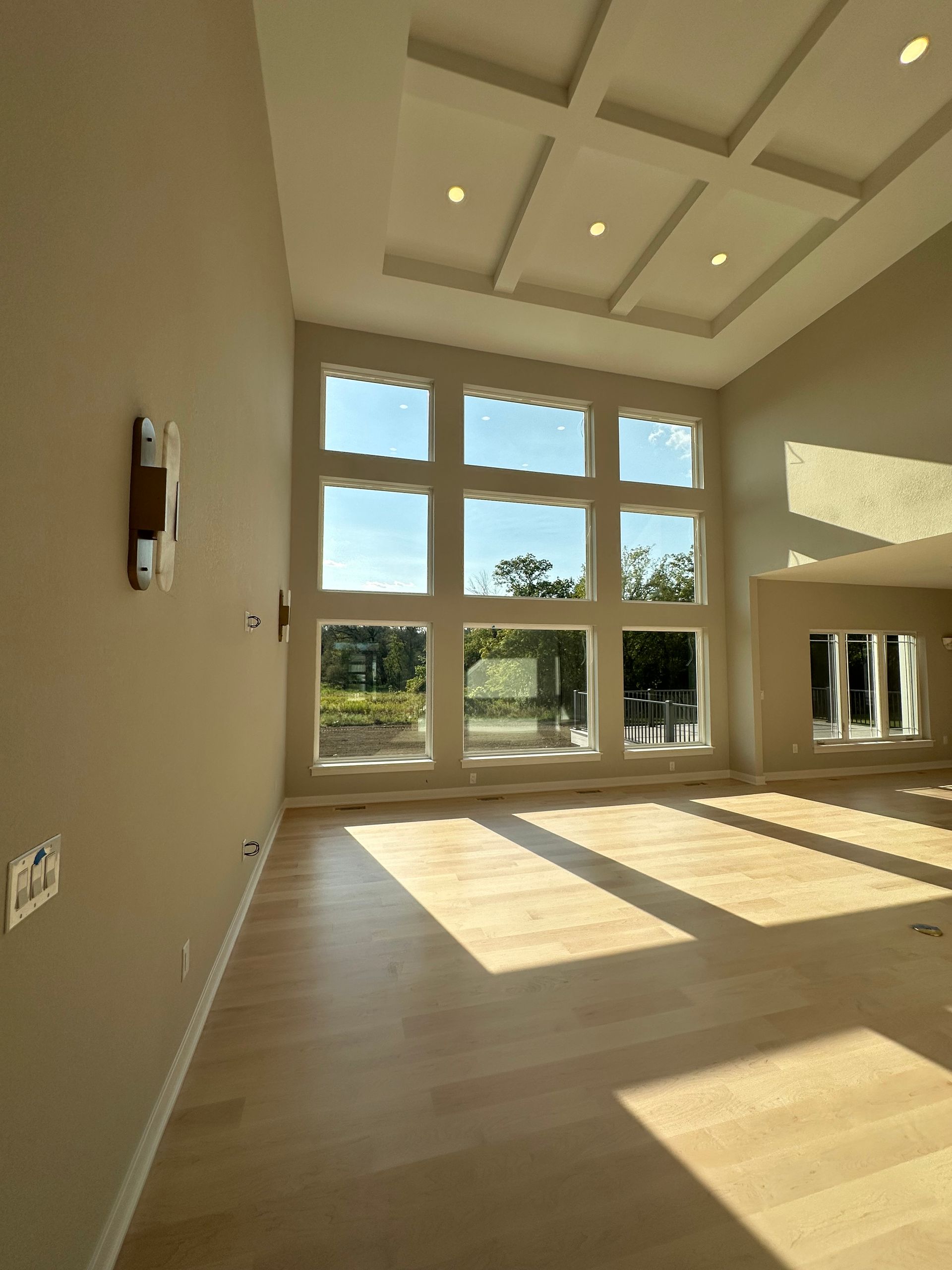 Spacious room with tall windows, light wood floors, coffered ceiling, and natural light.
