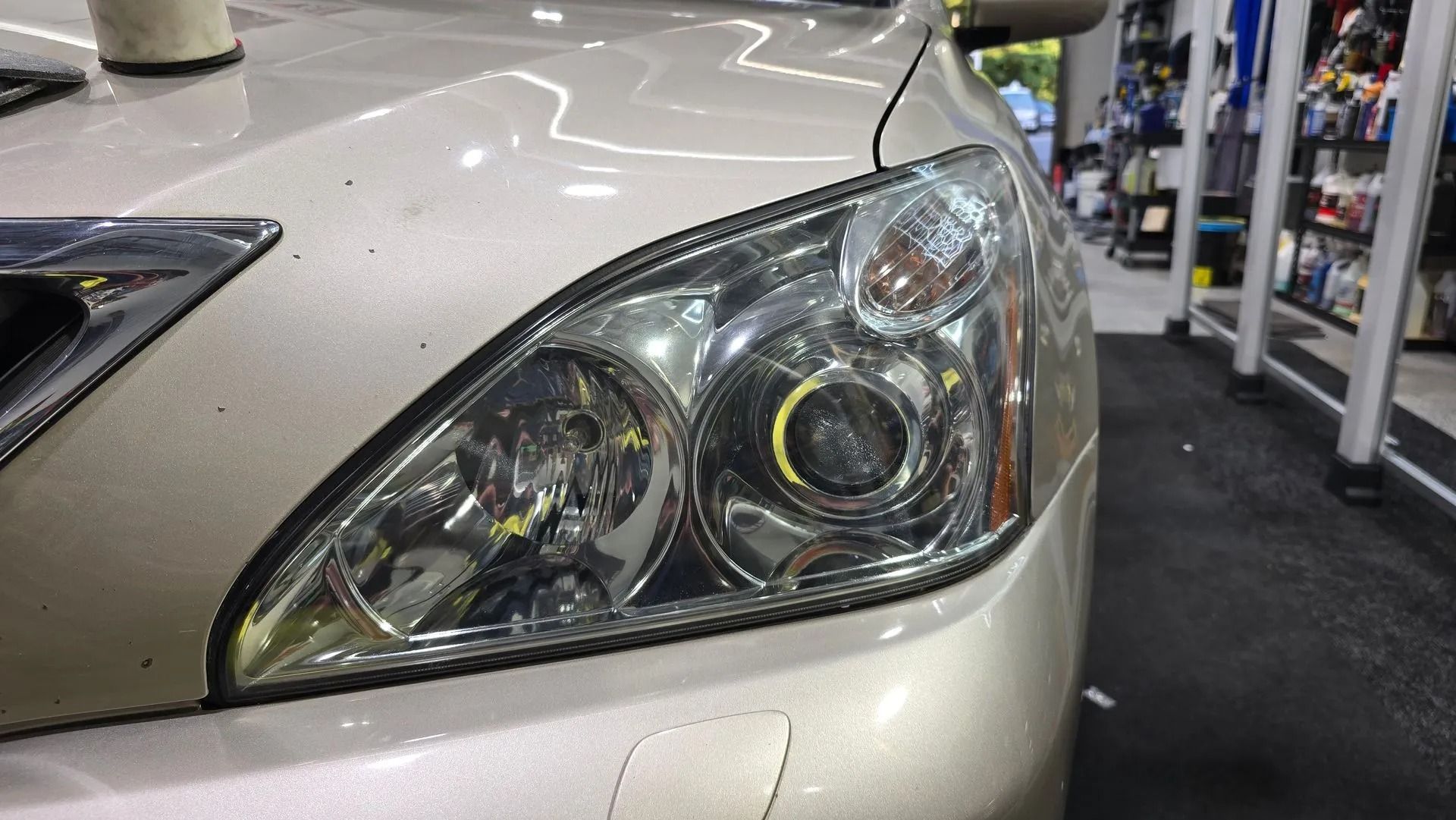 Close-up of a beige car's headlight assembly with internal projector lenses in an indoor garage setting.