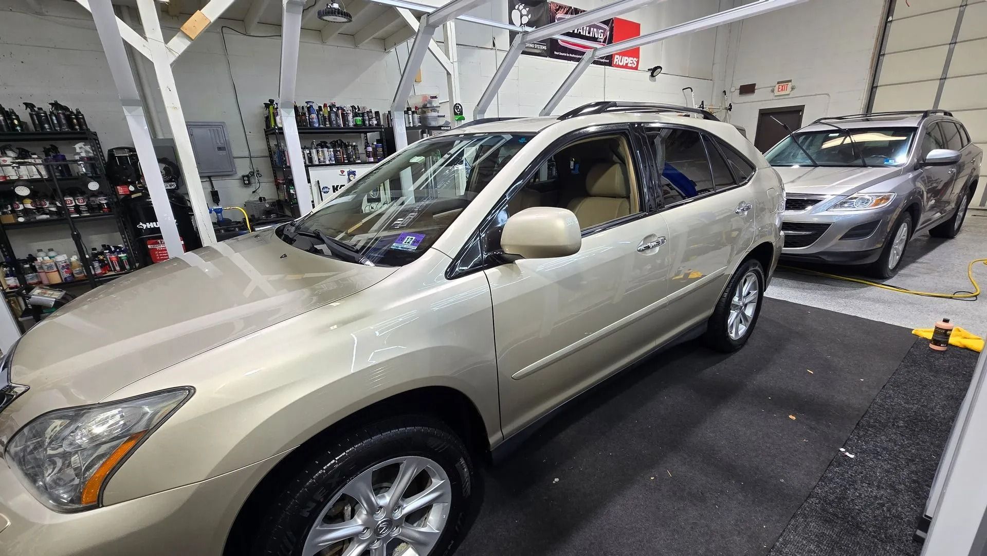 A gold SUV parked inside an auto shop next to another vehicle.