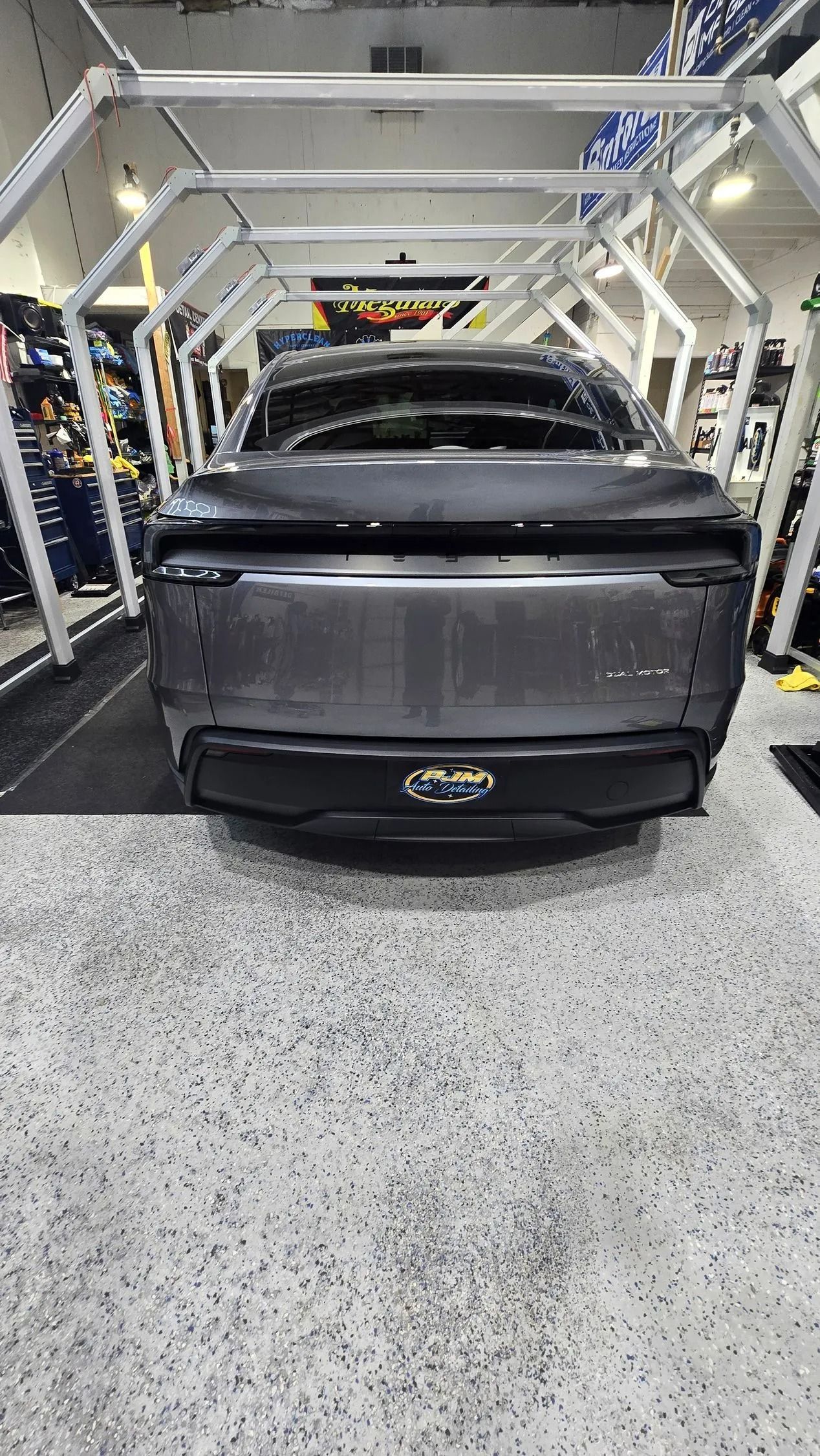 A grey electric vehicle positioned inside a car wash bay with metal arched framing.