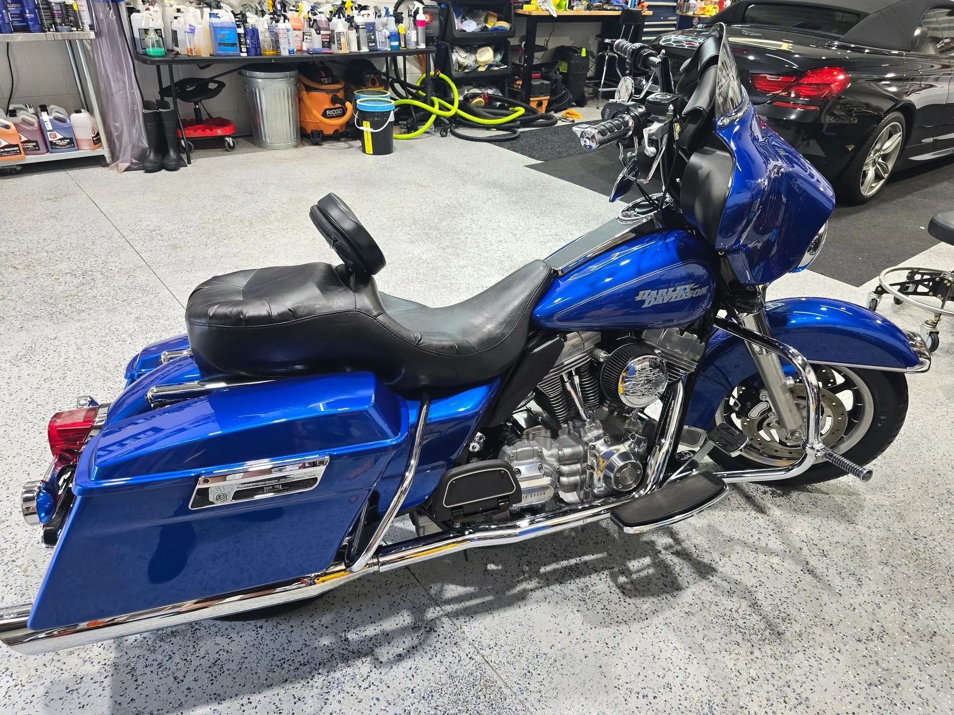 A bright blue Harley-Davidson touring motorcycle parked in a garage with black saddlebags and a backrest.