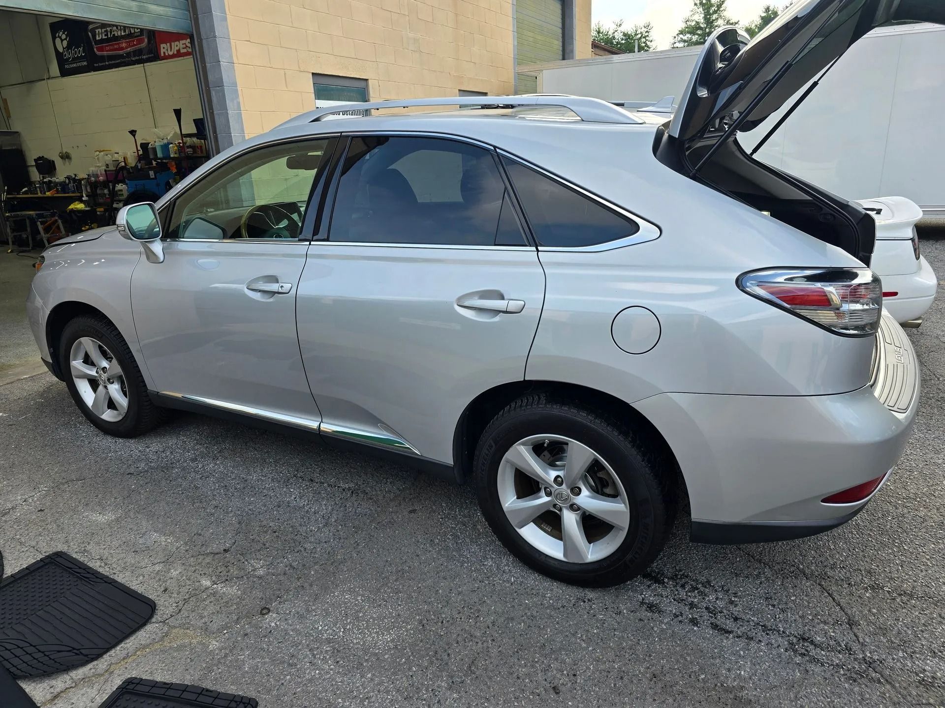 A silver Lexus RX SUV parked at an auto repair shop with its trunk open.