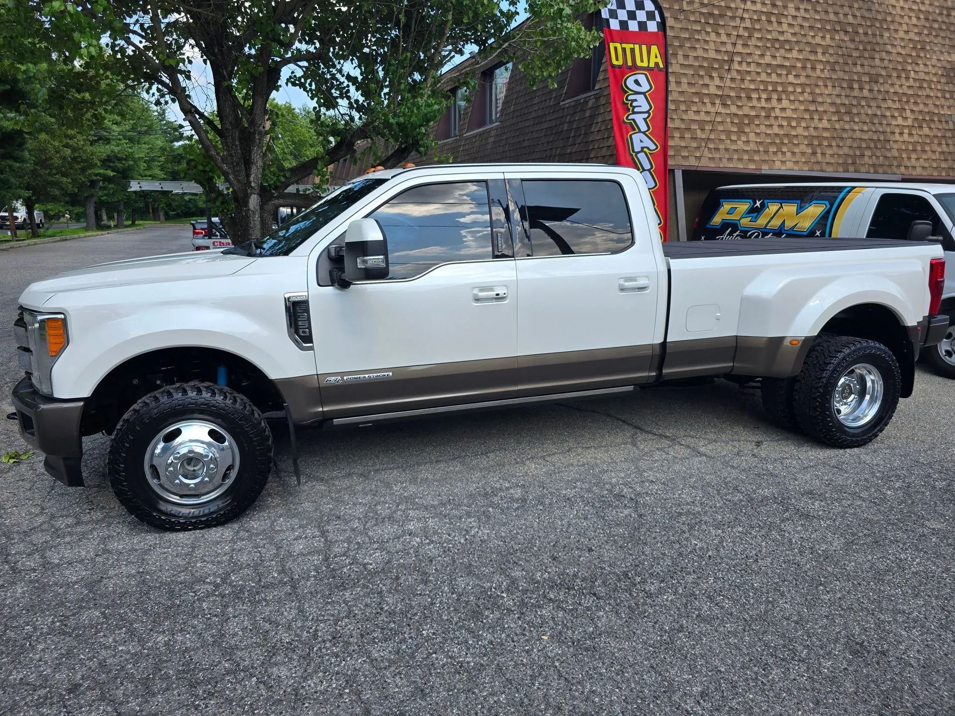 A white and tan Ford Super Duty dually pickup truck parked on an asphalt lot near a brick building.