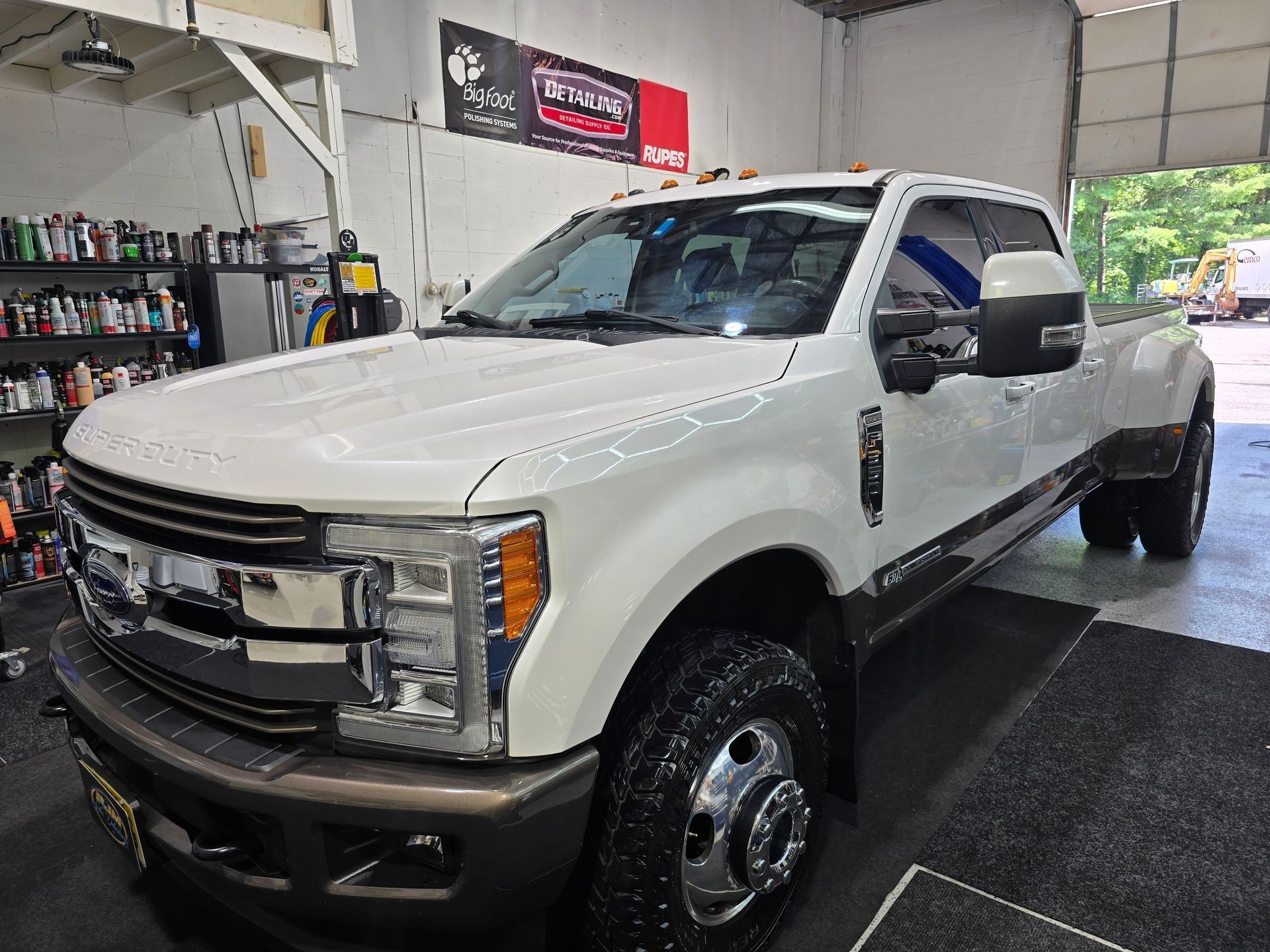 A white Ford Super Duty dually pickup truck parked inside a bright, well-organized automotive service garage.