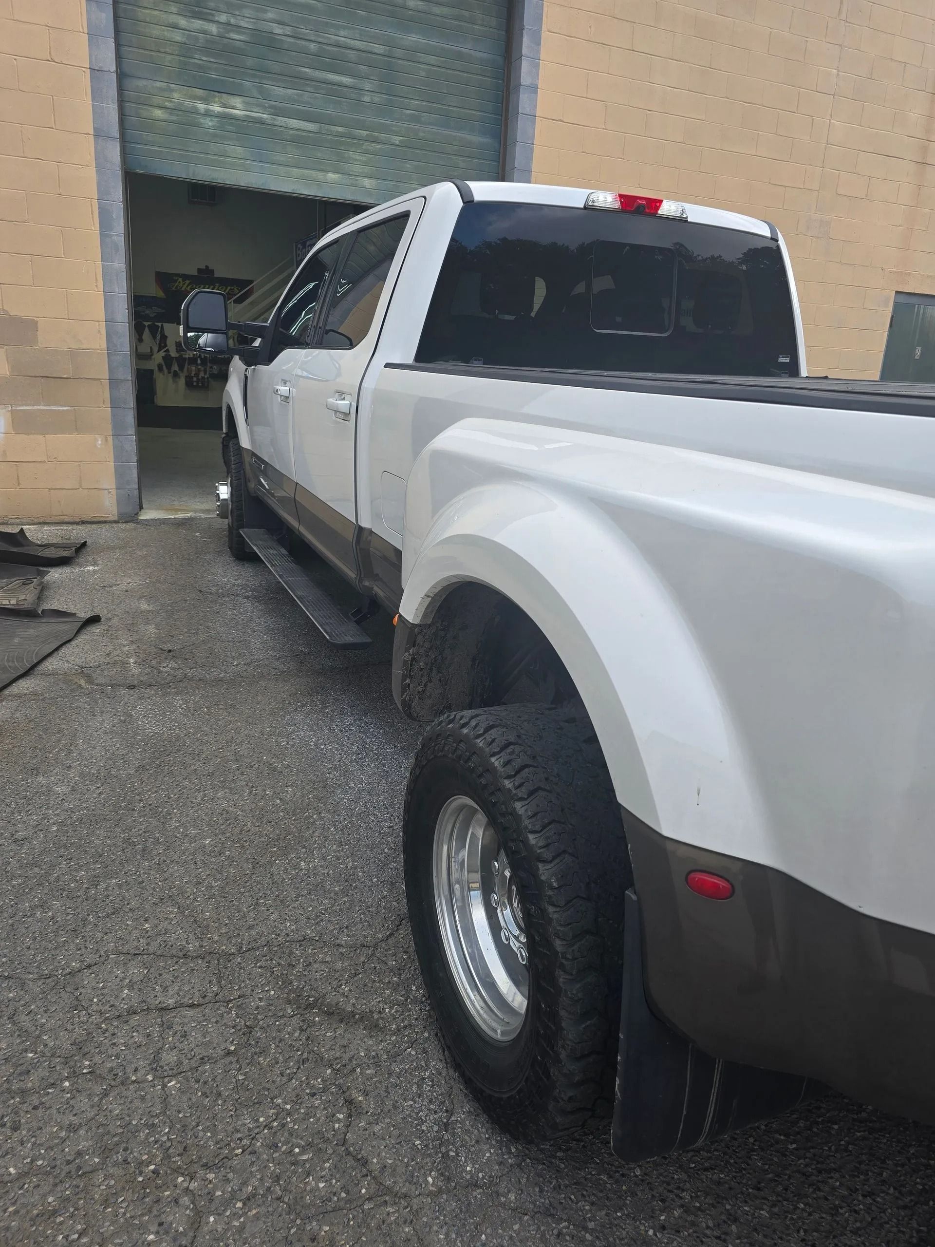 A white Ford dually pickup truck parked next to a building entrance on a gravel surface.