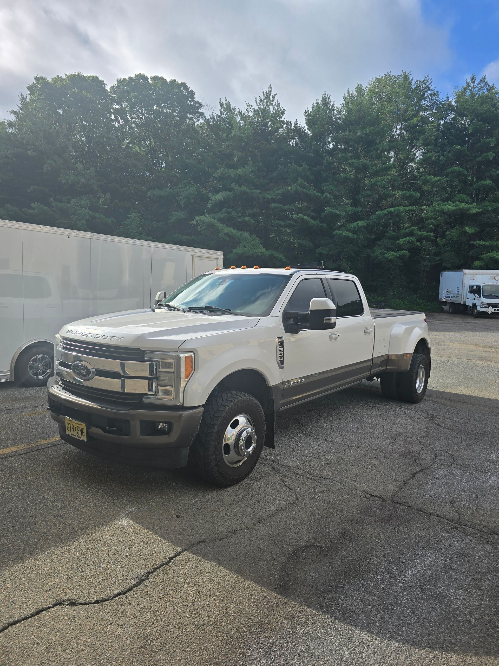 A white Ford F-350 dually pickup truck with bronze lower paneling parked on a gravel lot under a cloudy sky.
