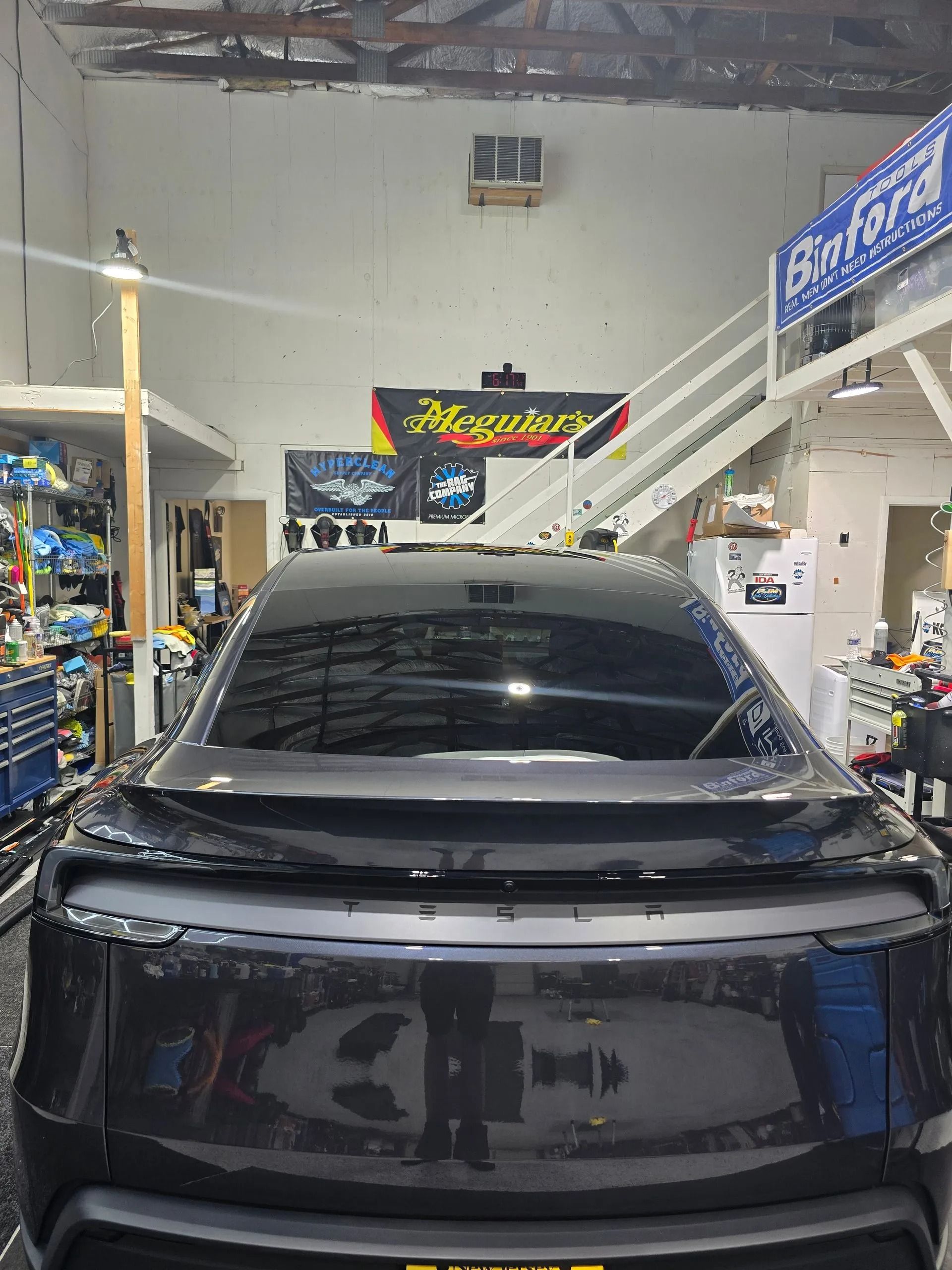 A rear view of a black sedan parked inside an auto shop with white stairs and signage in the background.