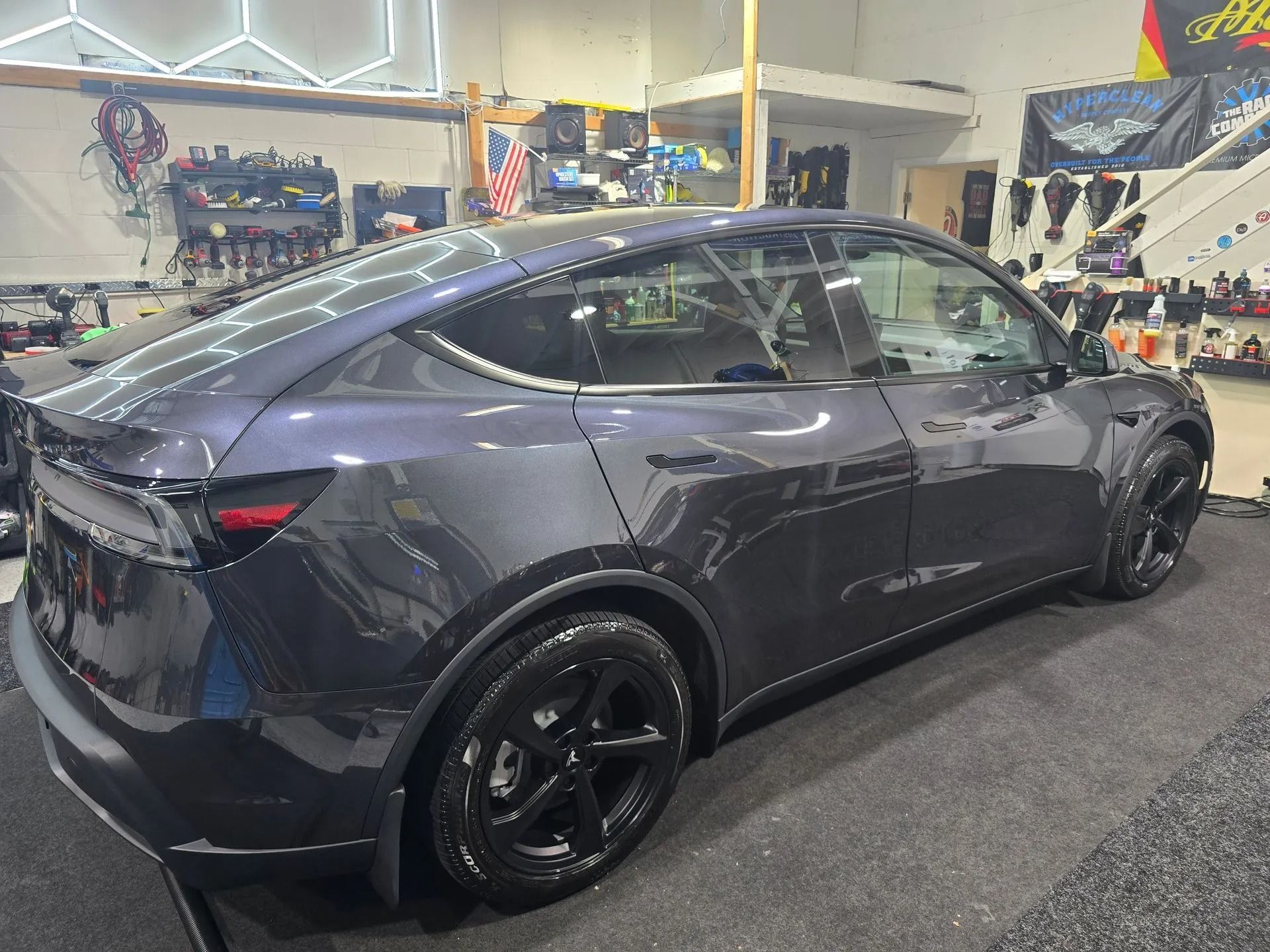 A dark grey Tesla Model Y parked inside a garage, featuring black wheels and tinted windows.