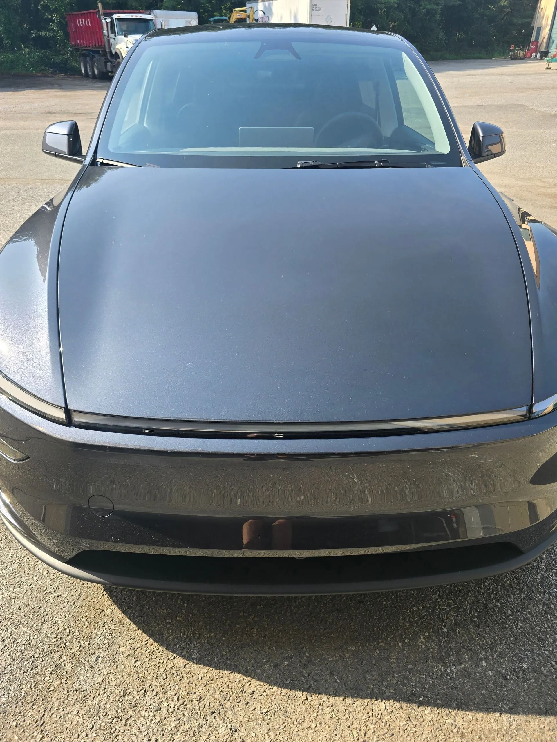 A black Tesla parked on a gravel lot, viewed head-on from the front.
